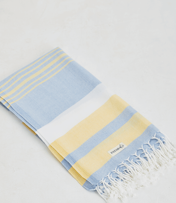 a pale yellow, blue and white lightweight towel is folded and layed flat on white background
