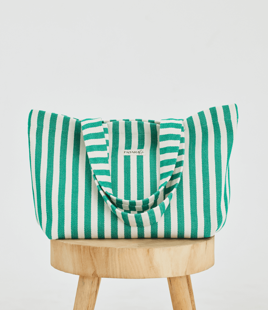  a green and white striped tote bag placed up right on a stool