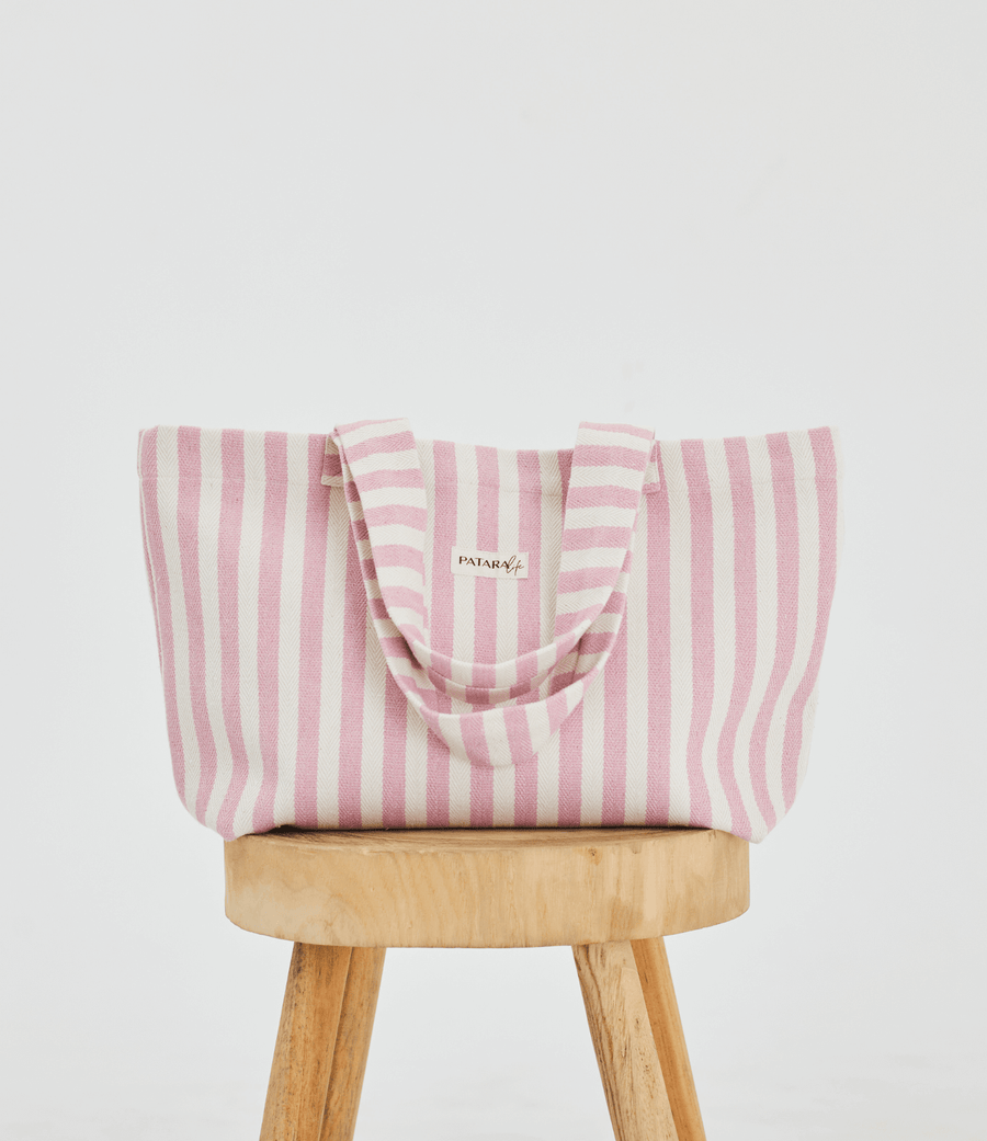  a light pink and white striped tote bag placed up right on a stool