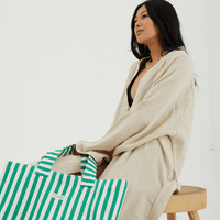 a girl sitting on a stool with a green and white striped tote bag positioned by her leg