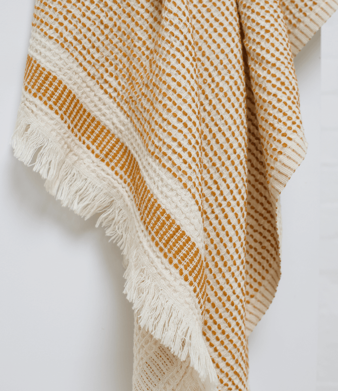 A mustard turkish beach towel with dotted thread hanging on the high stand
