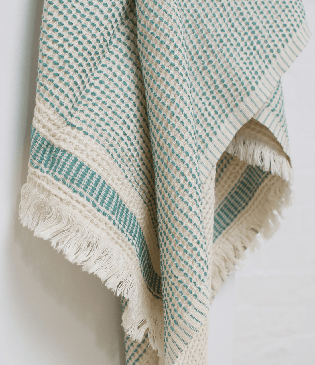 A sage green turkish beach towel with dotted print hanging on the high stand